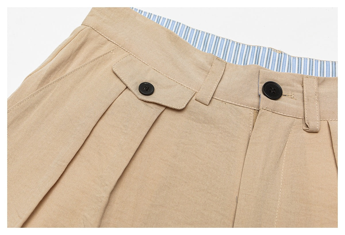 Close-up of tan trouser front waistband with pleats, black buttons, belt loops, and striped inner lining.