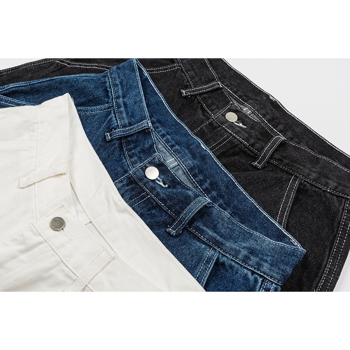 Close-up of white, blue, and black denim shorts overlapping, showing waistbands, belt loops, and buttons.