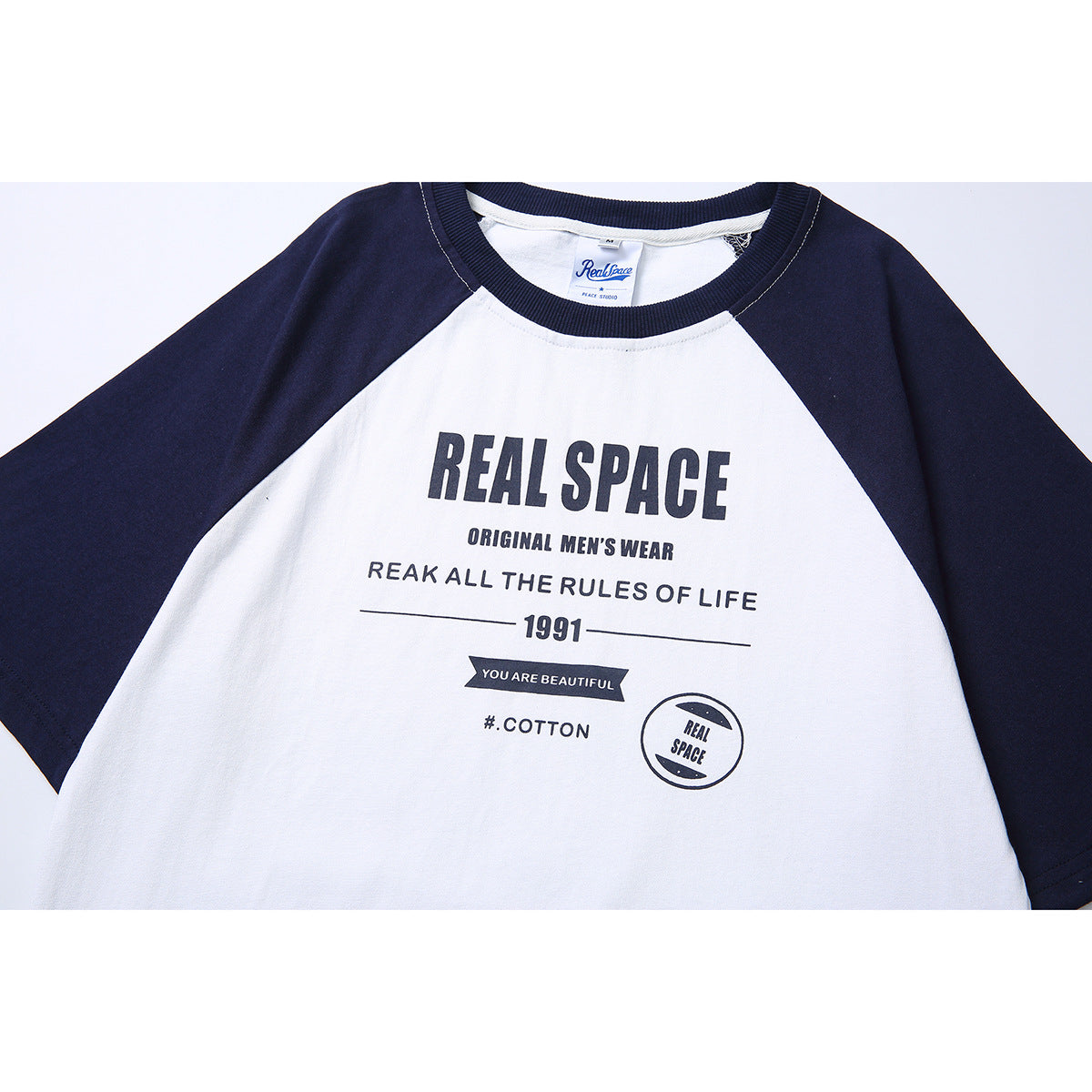 Close-up of a white raglan T-shirt with navy sleeves and a large dark printed graphic on the chest.