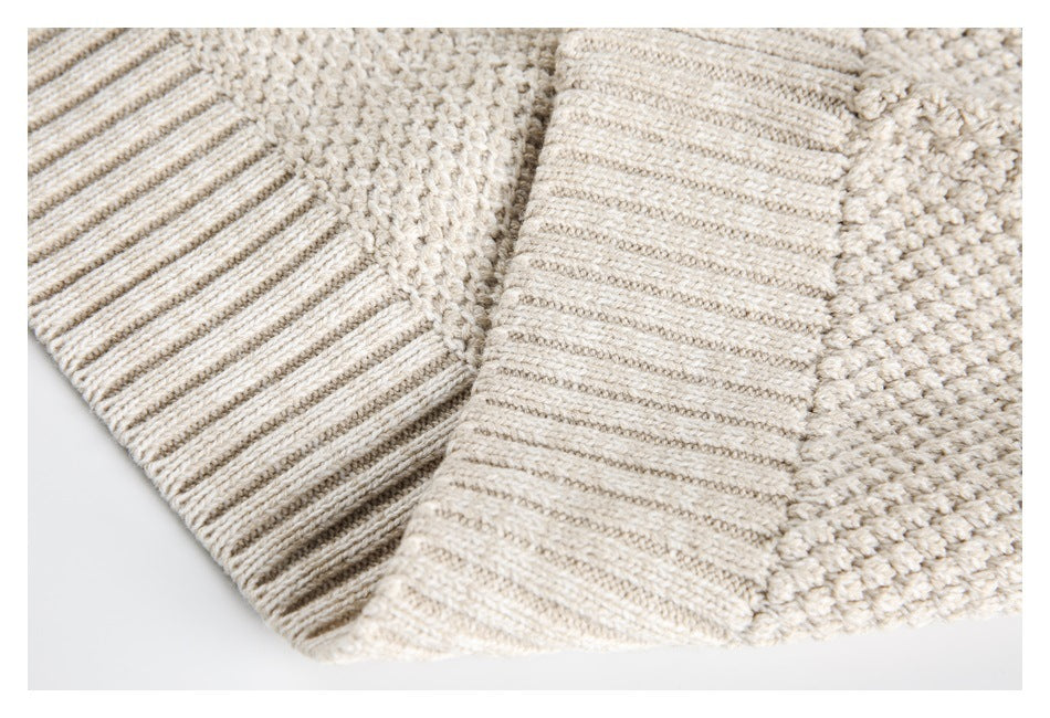 Close-up of a cream knit sweater showing ribbed trim beside its chunky textured body.