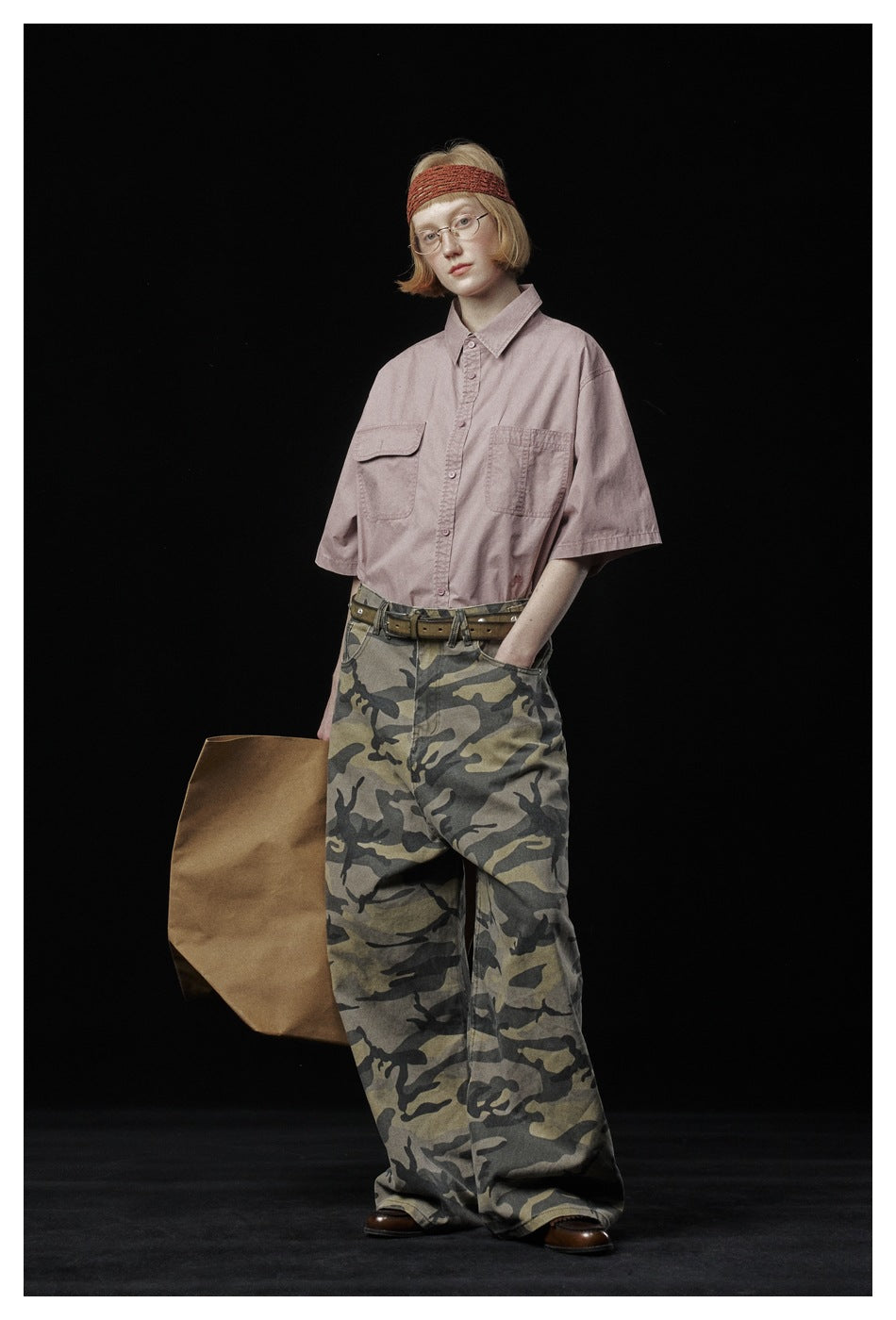 Model wearing a dusty pink two-pocket short-sleeve shirt tucked into loose camouflage trousers.