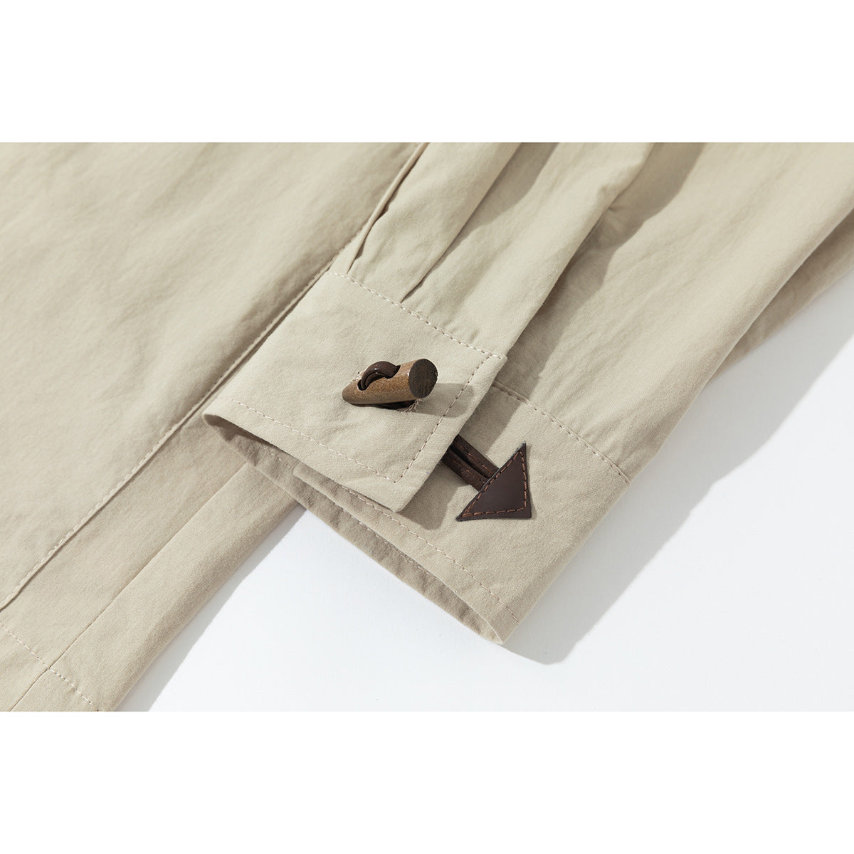 Close-up of a beige jacket sleeve cuff with a brown toggle and triangular tab detail.