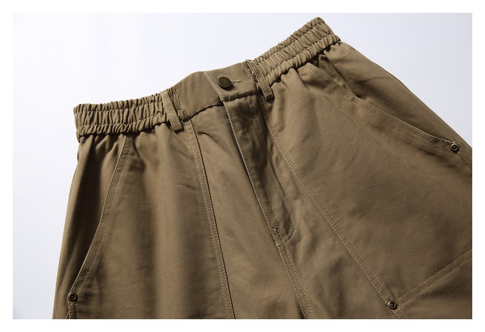 Close-up of olive-brown trousers showing an elastic waistband, button fly, and stitched front pockets.