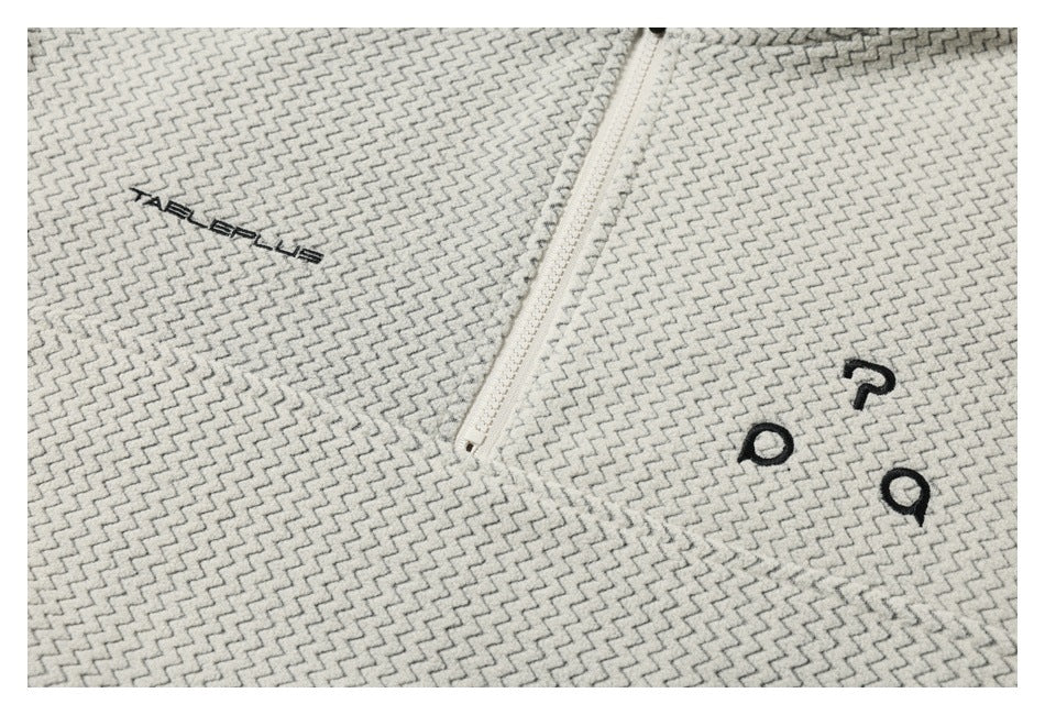 Close-up of cream and gray zigzag-patterned fabric with a white zipper and small black embroidered lettering.