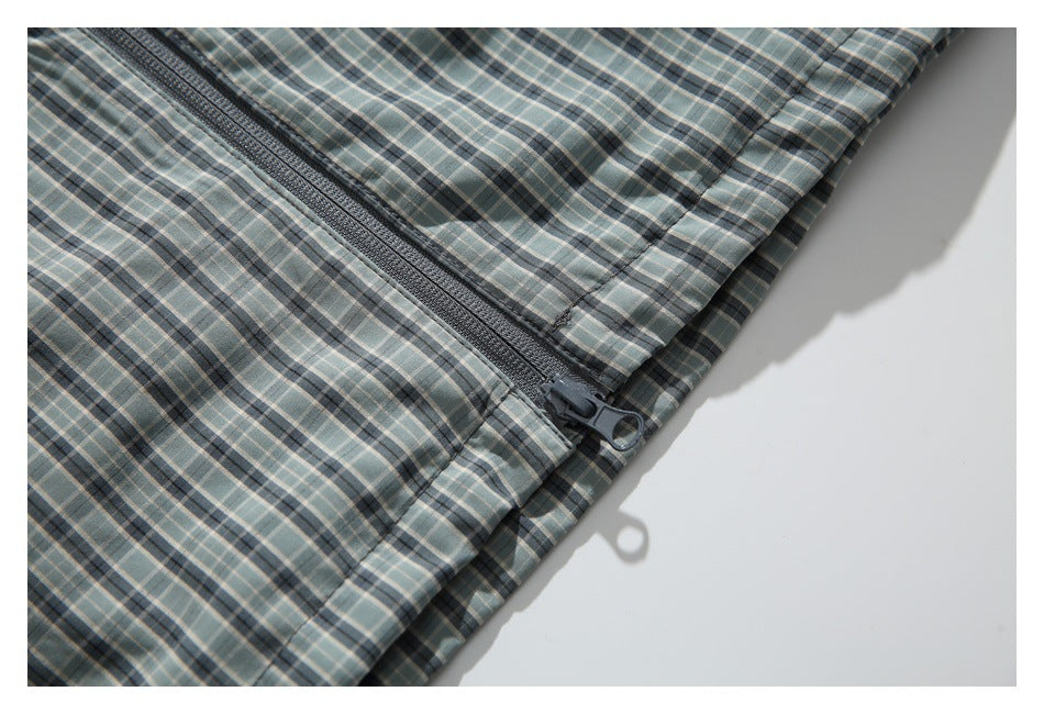 Close-up of a dark zipper and pull on gray-green plaid jacket fabric.