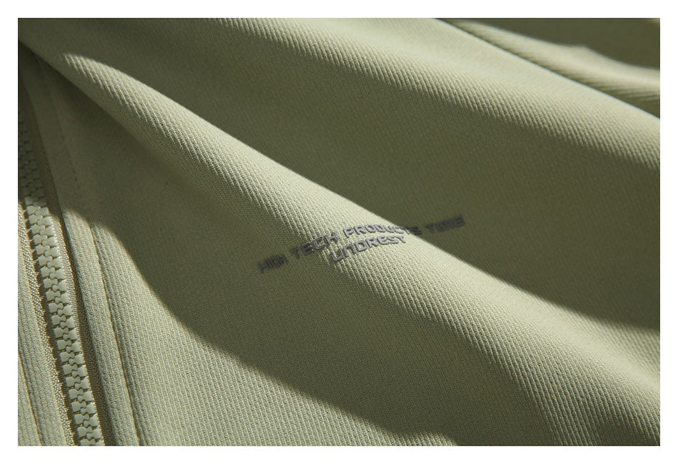 Close-up of textured sage-green fabric with a zipper edge and small dark lettering printed on the jacket.