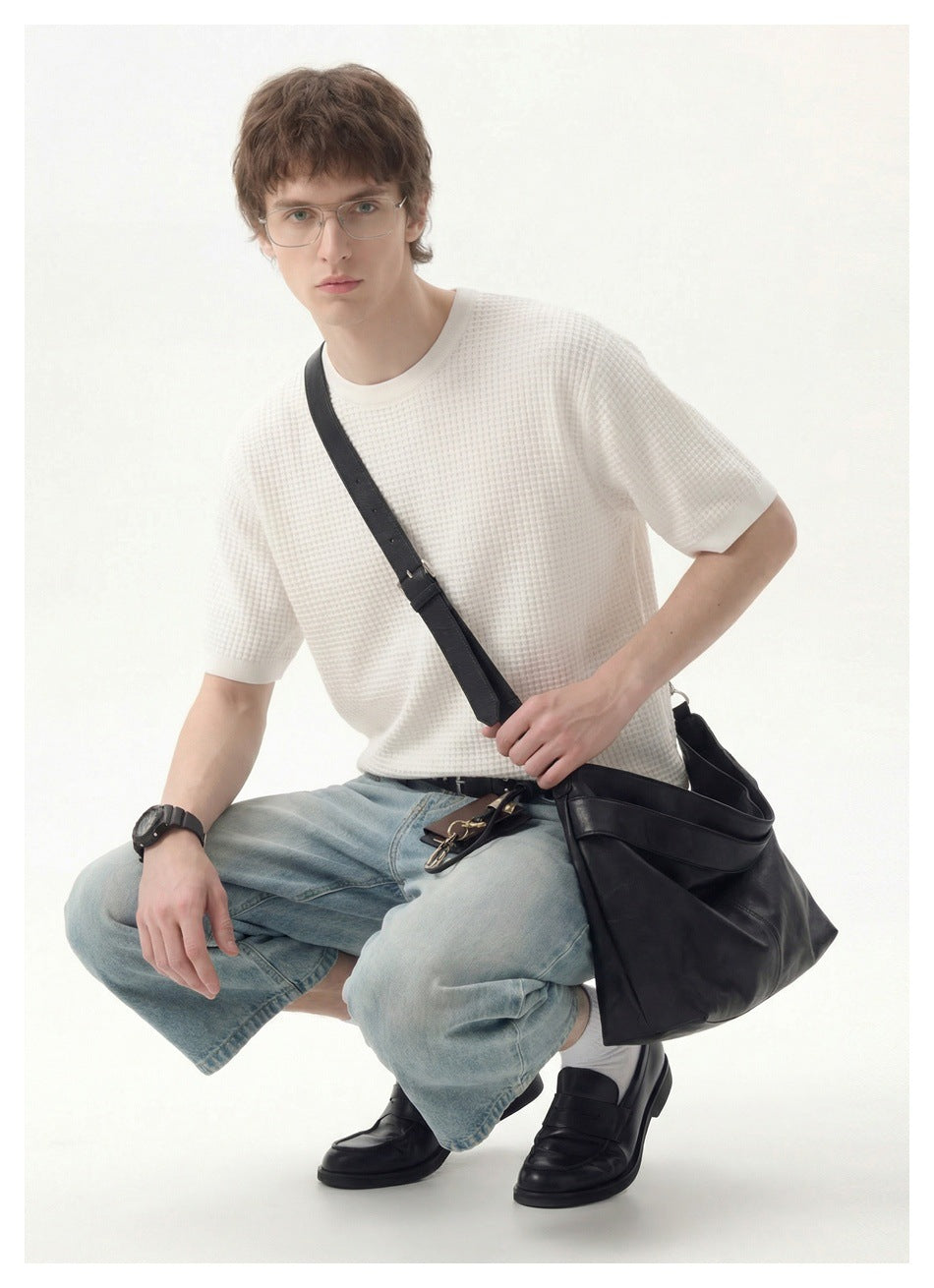 Seated model wearing a white textured short-sleeve shirt and light-wash denim shorts with a black shoulder bag.