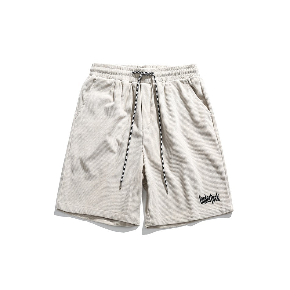 Beige corduroy-style shorts with elastic waist, patterned drawstring and black embroidered text, flat lay front view