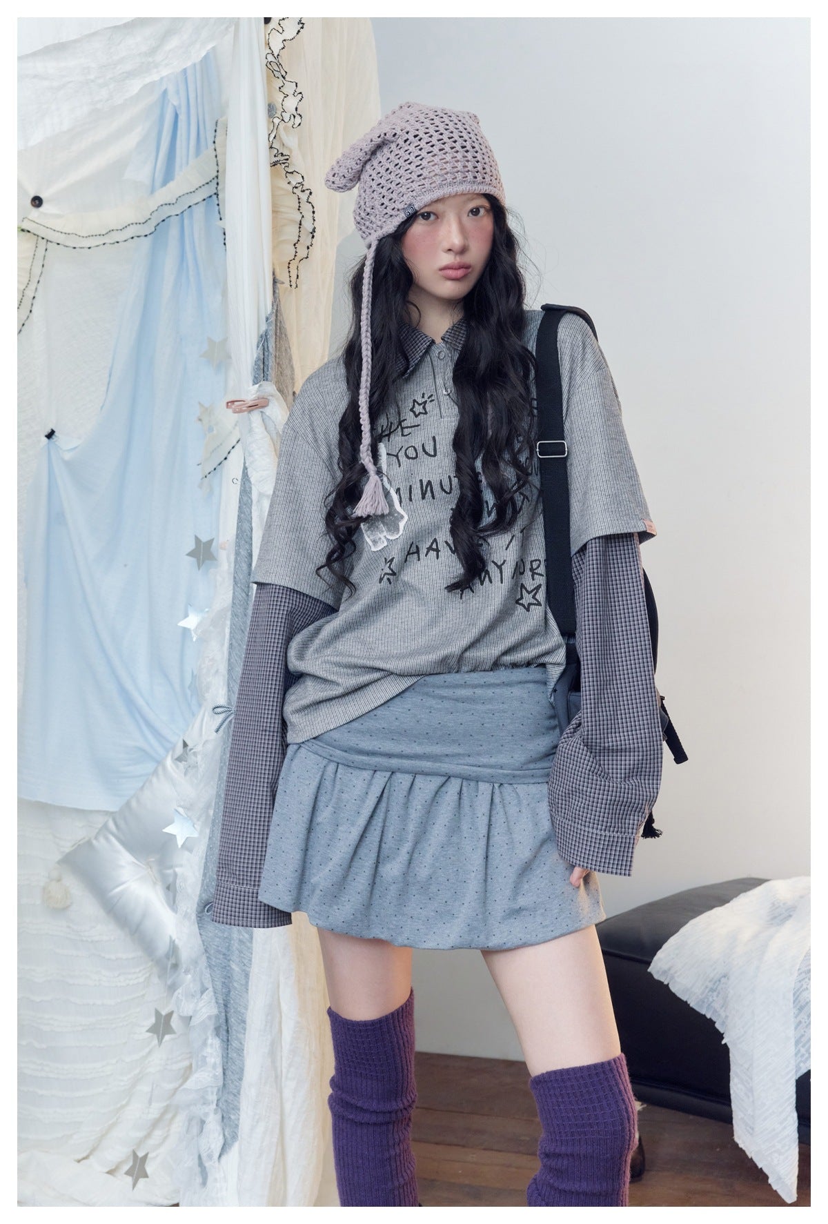 Front view of a model in a layered gray printed top, checked sleeves, gray mini skirt, and lavender knit hat.
