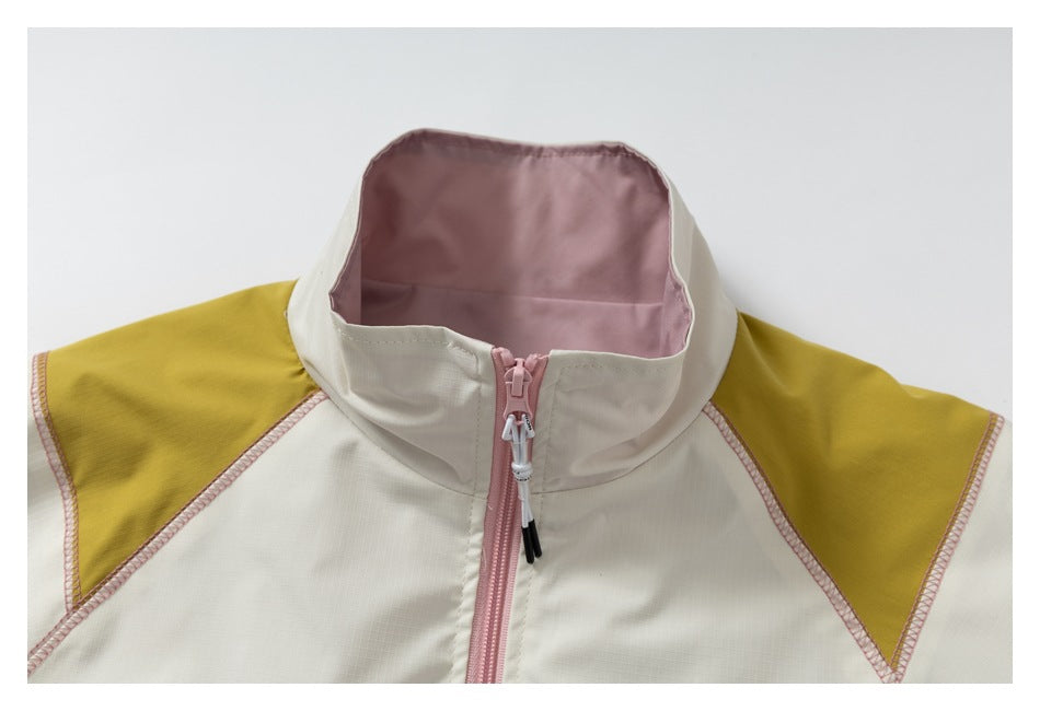 Close-up of a cream jacket's high collar, pink lining and front zipper, with mustard shoulder panels and pink stitching.
