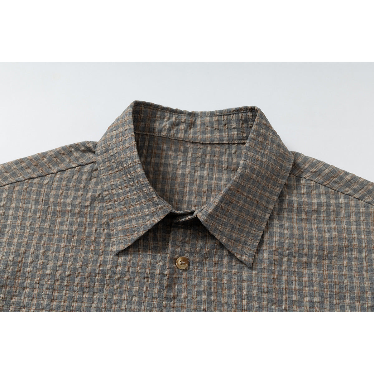 Close-up of a gray-brown plaid shirt collar and top button.