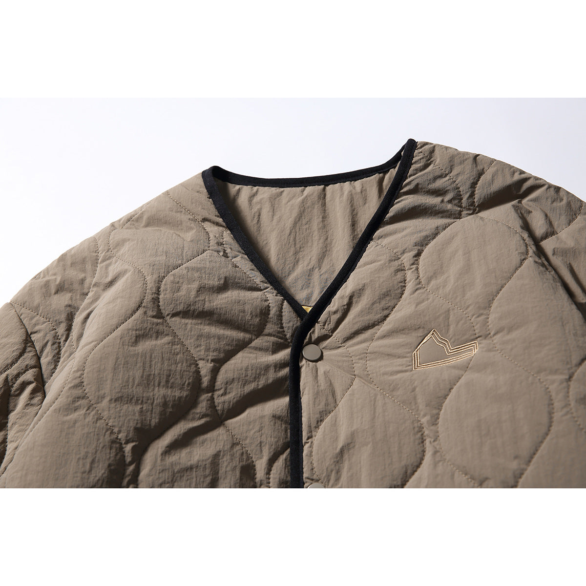 Close-up of the taupe jacket's black-trimmed V-neck, snap closure and small embroidered chest emblem.