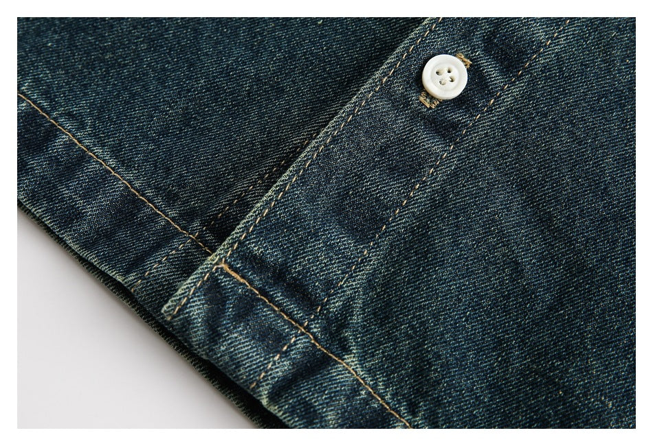 Close-up of dark indigo denim with tan stitching and a white button.