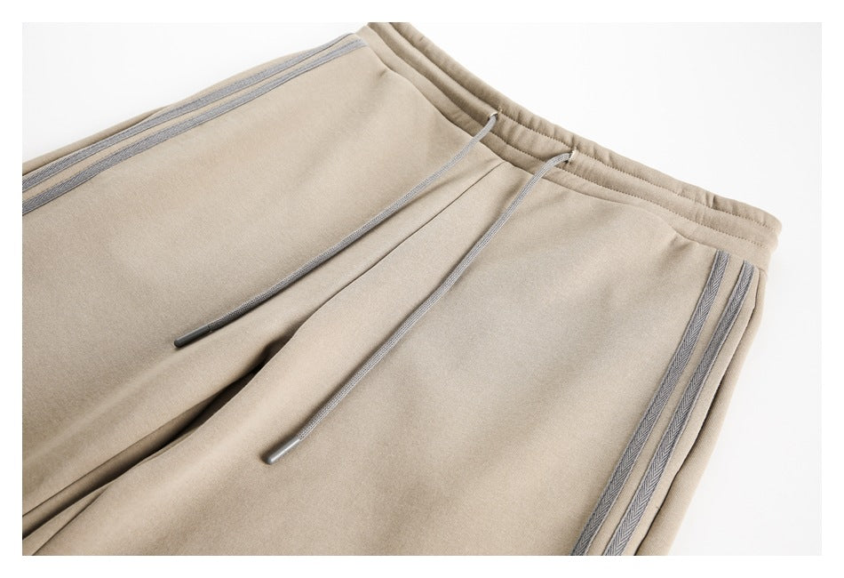 Close-up of beige pants showing the elastic waistband, gray drawstrings, and striped side trim.