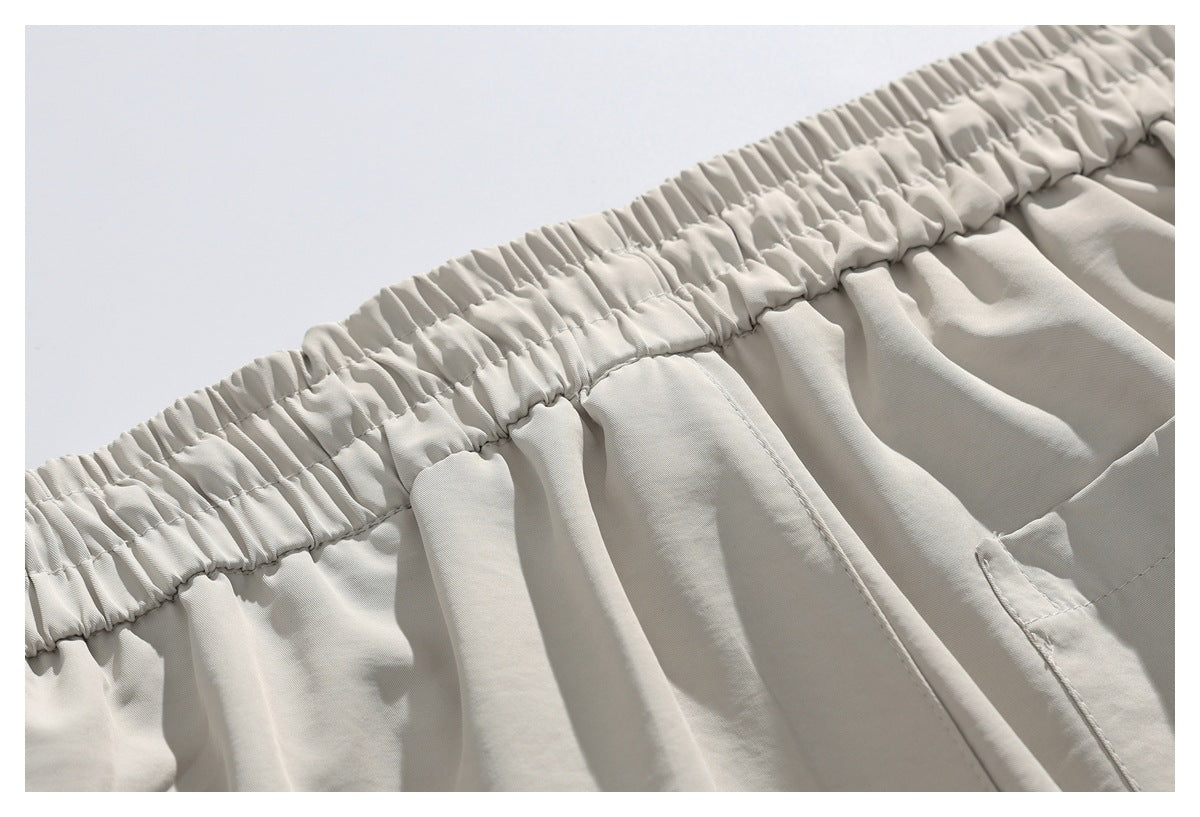 Close-up of light beige trousers showing a gathered elastic waistband and stitched fabric panels.