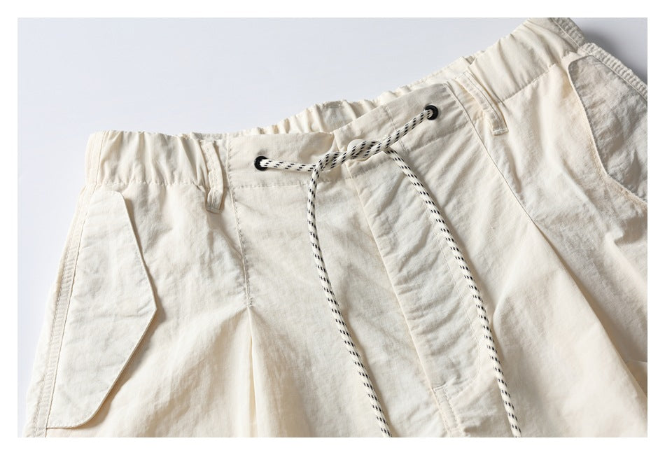 Close-up of off-white shorts showing the elastic waistband, black-and-white drawcord, eyelets and front pocket seams.