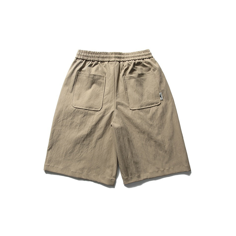Back view of beige shorts with an elastic waistband, two patch pockets, and a small side tab.