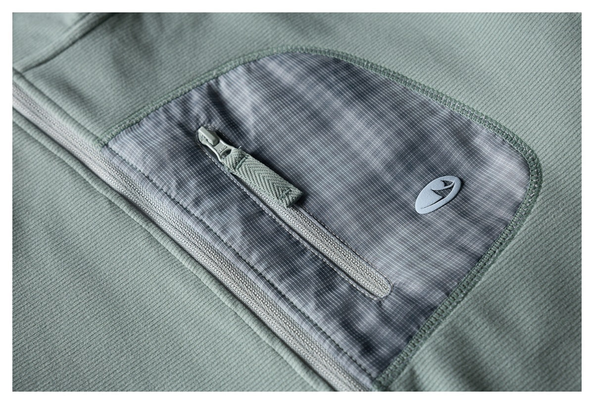 Close-up of the jacket’s gray grid-patterned zip pocket and small emblem against sage-green fabric.