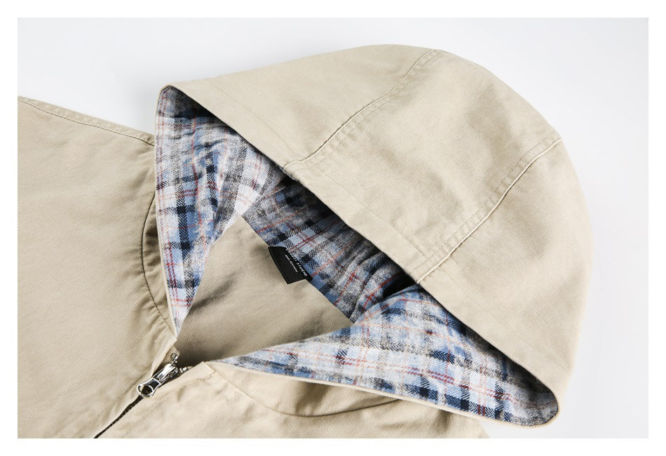 Close-up of a beige jacket hood with blue, gray, and rust plaid lining and a metal zipper.