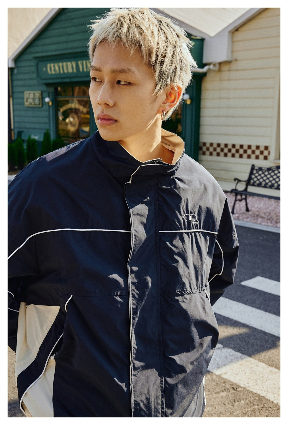 Closer front view of a navy jacket with white piping, a stand collar, and a chest pocket, worn by a model.