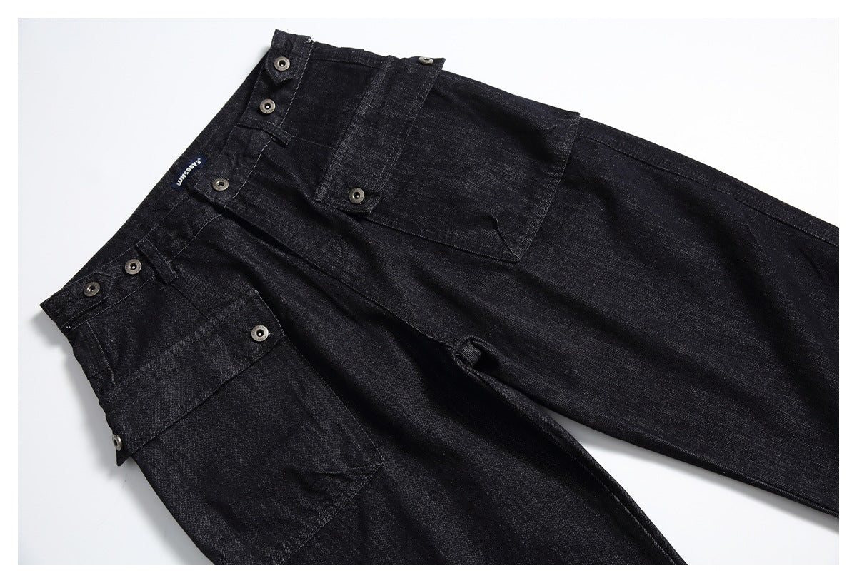 Angled flat lay of black denim trousers showing the front, buttoned waistband tabs and utility pockets.