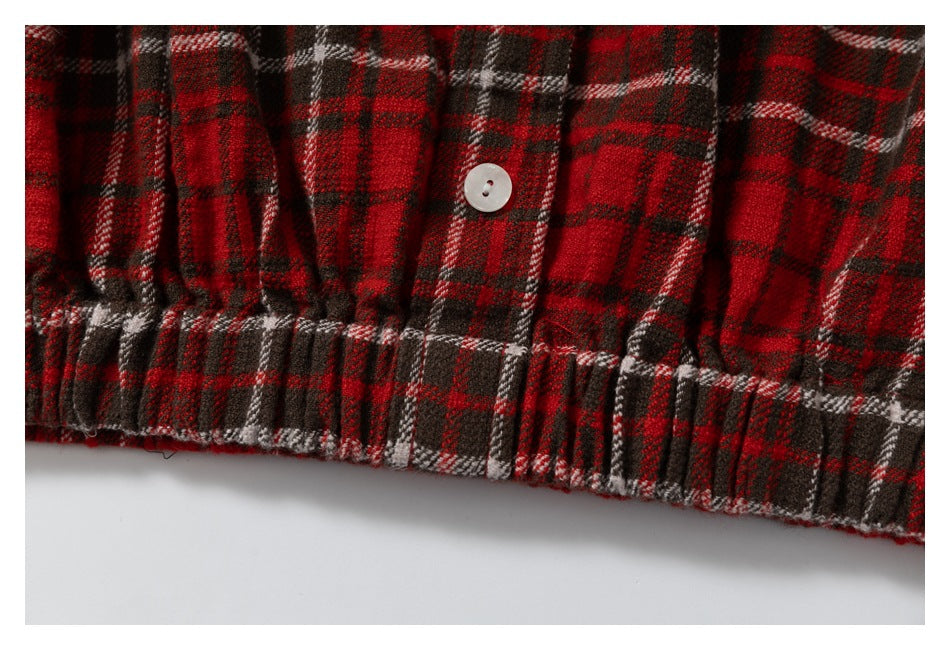 Close-up of a red, black, and white plaid garment with a white button and gathered edge.