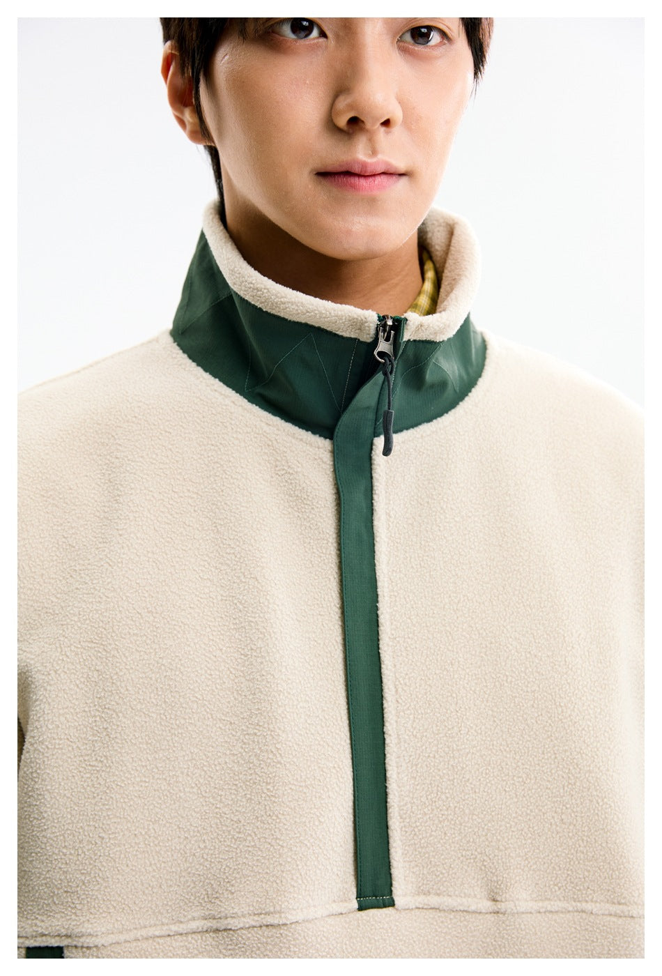 Close-up of a model wearing the cream fleece pullover, showing its dark green zip-front trim and high collar.