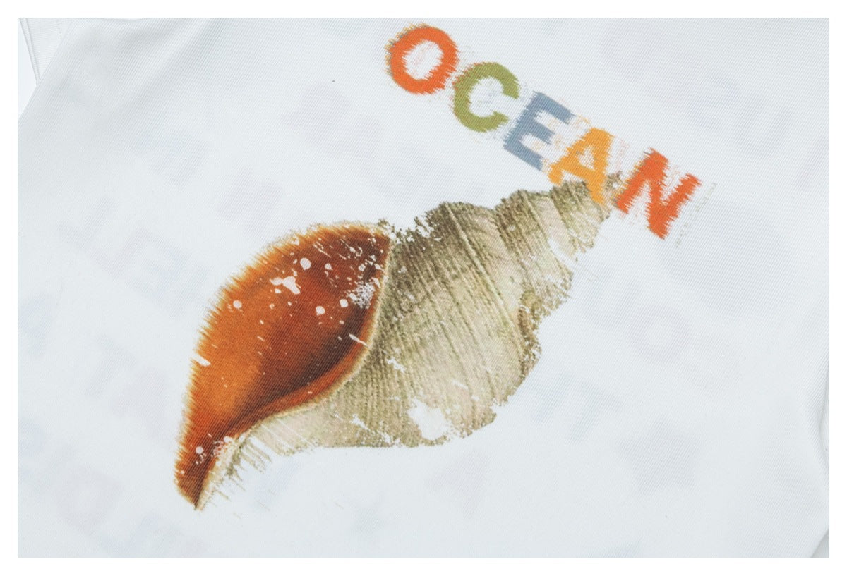 Close-up of a seashell print and partial multicolored lettering on white fabric.