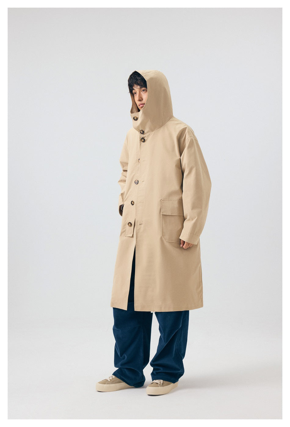 Model wearing a button-front beige coat with the oversized hood raised and hands in the pockets.