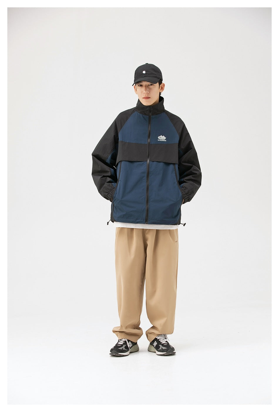 Model wearing a navy and black color-block zip jacket with a high collar and loose tan trousers, front view.