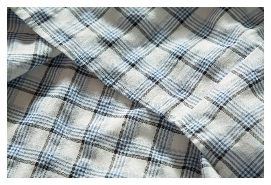 Close-up of white blue and charcoal plaid fabric draped in overlapping folds with a stitched edge.
