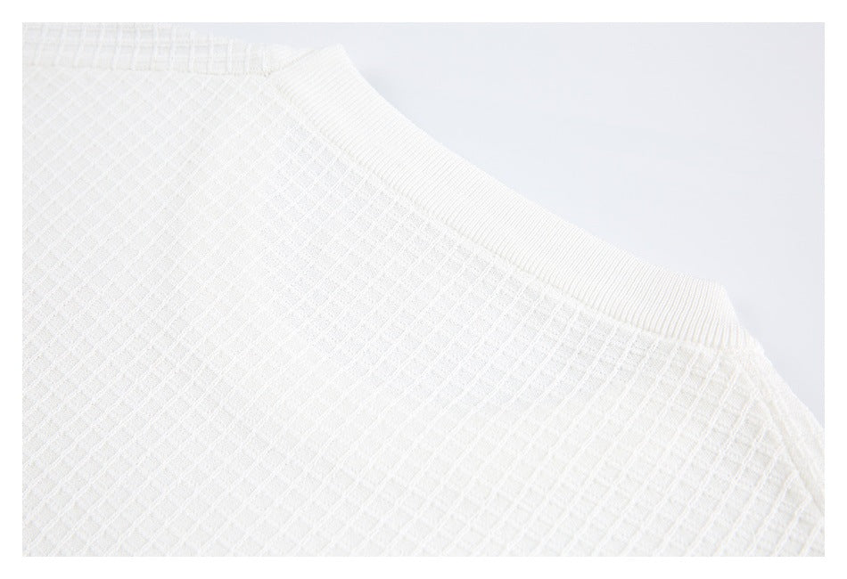 Close-up of a white sweater's ribbed crew neckline and raised grid-knit body.