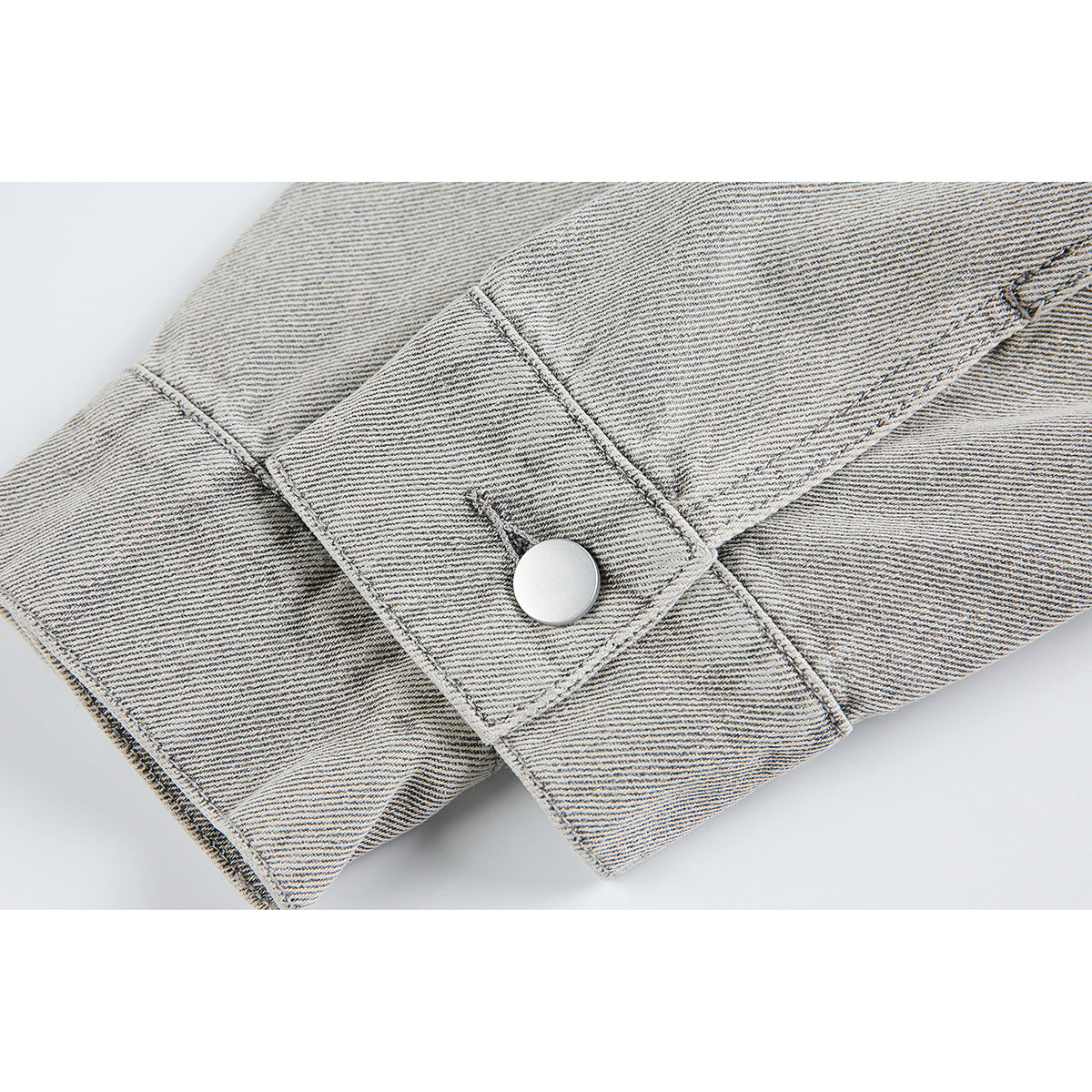 Close-up of a light gray jacket cuff with a silver snap and visible stitching.
