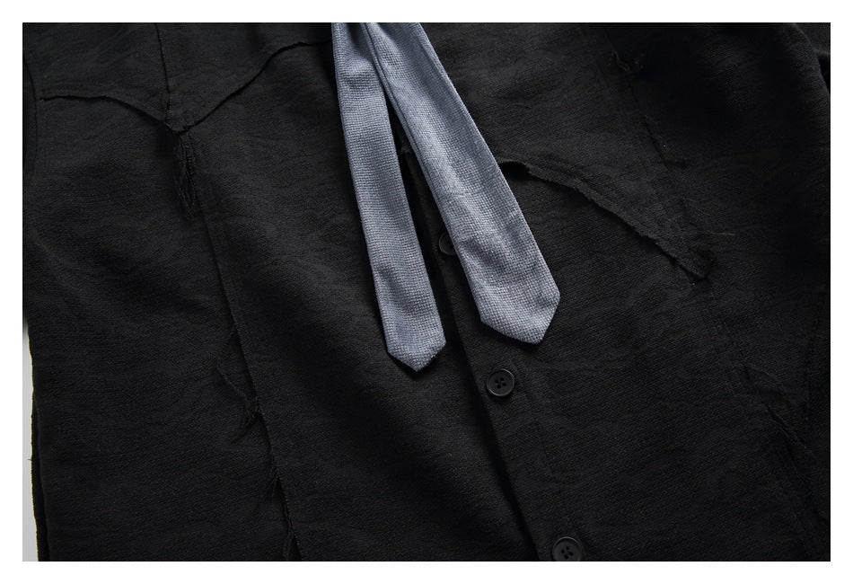 Close-up of a black button-up shirt with a light gray tie and visible chest pocket.