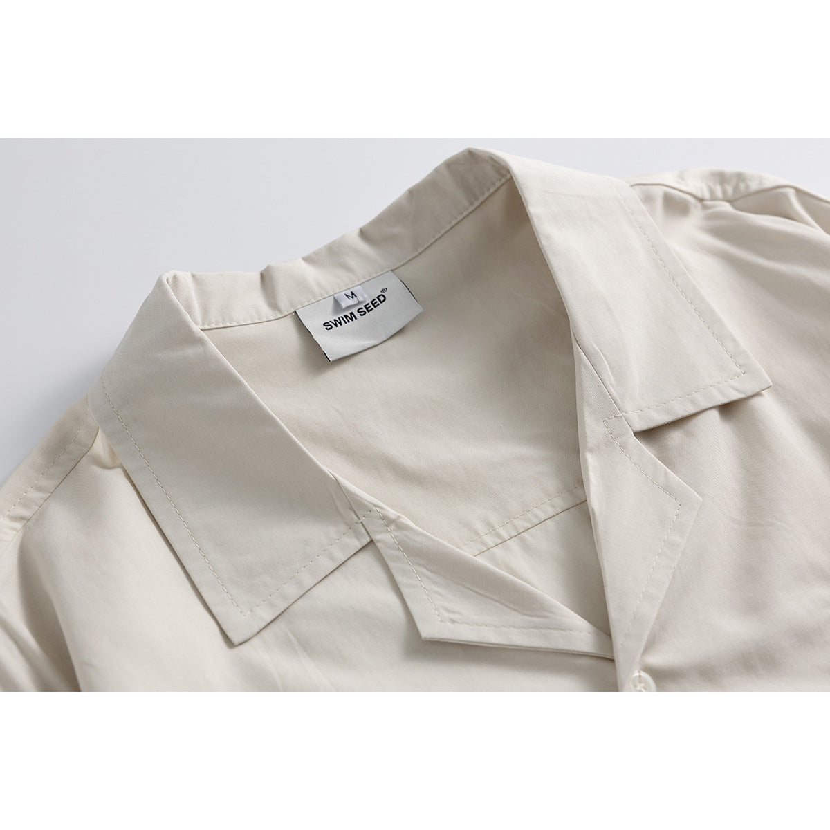 Close-up of an ivory shirt's open camp collar, stitching, and sewn-in neck label.