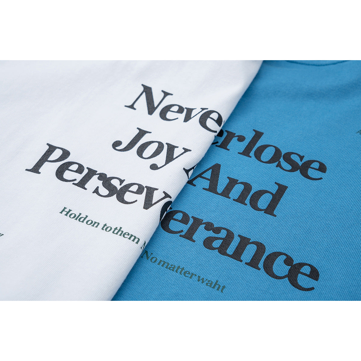 Close-up of overlapping white and blue T-shirts showing large black typography and smaller printed text.
