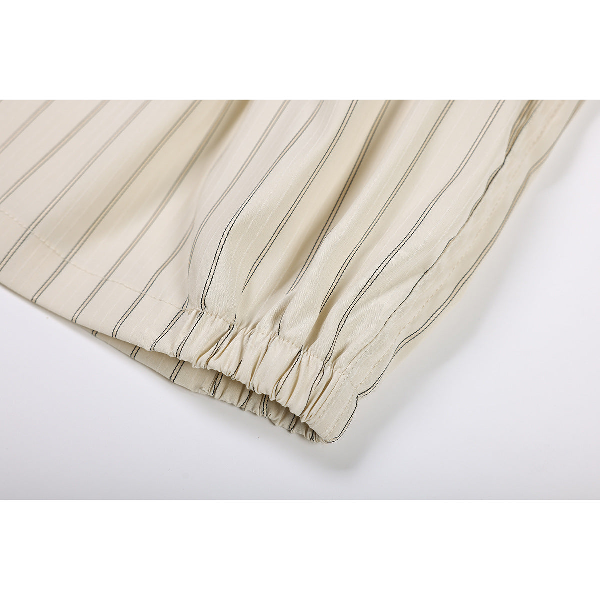 Close-up of the gathered elastic hem on cream shorts with thin dark vertical stripes.