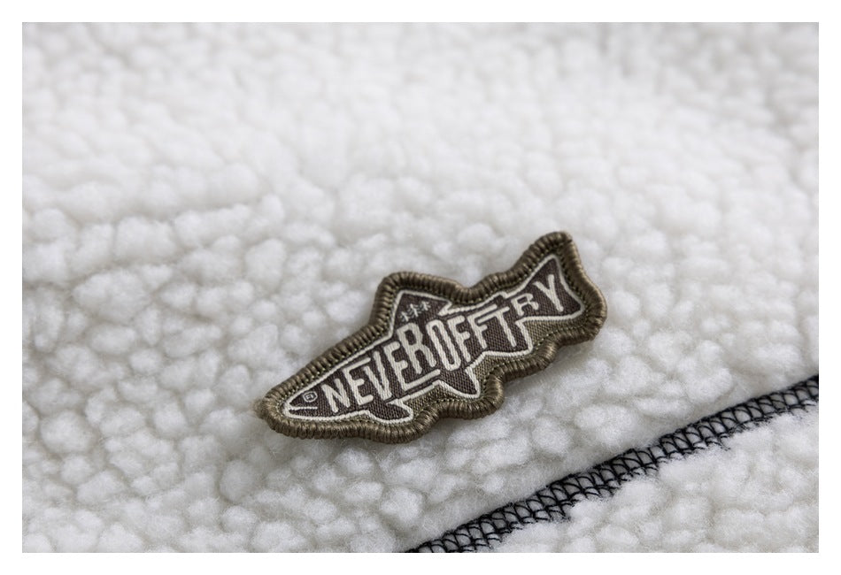 Close-up of an embroidered English-lettered patch and dark overlock stitching on the ivory sherpa jacket.