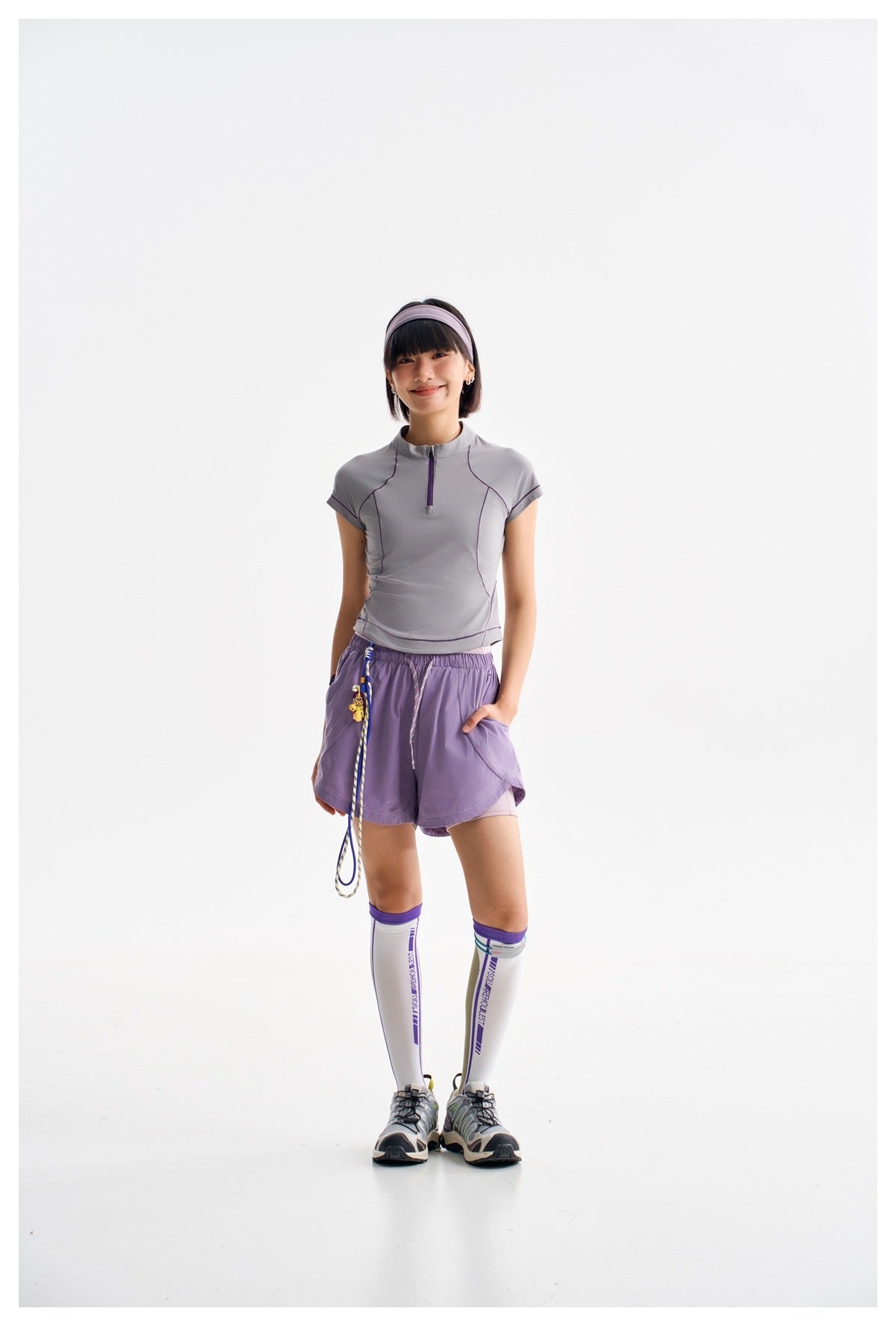 Full-length model in a light gray-lavender zip-neck top, purple shorts, knee-high socks, and sneakers.
