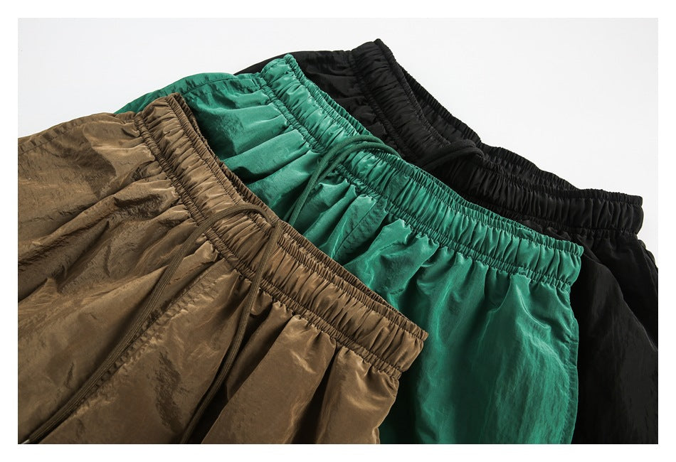 Three overlapping pairs of shorts in brown, emerald green, and black, showing their elastic waistbands.