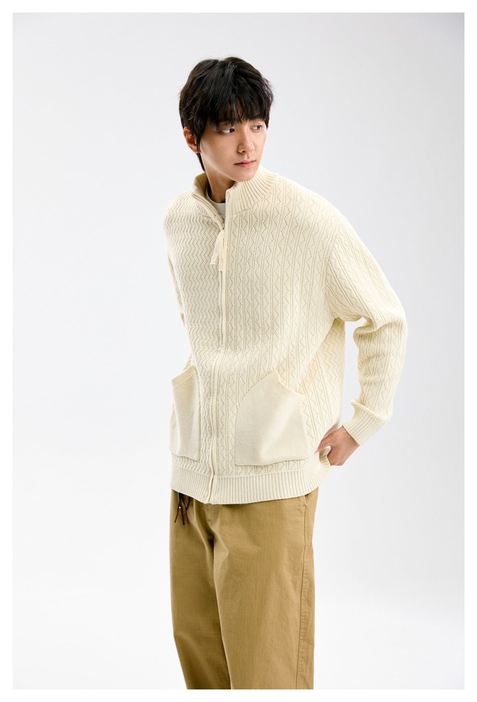 Model wearing a cream textured knit cardigan with a high collar, front zip, and two large patch pockets.