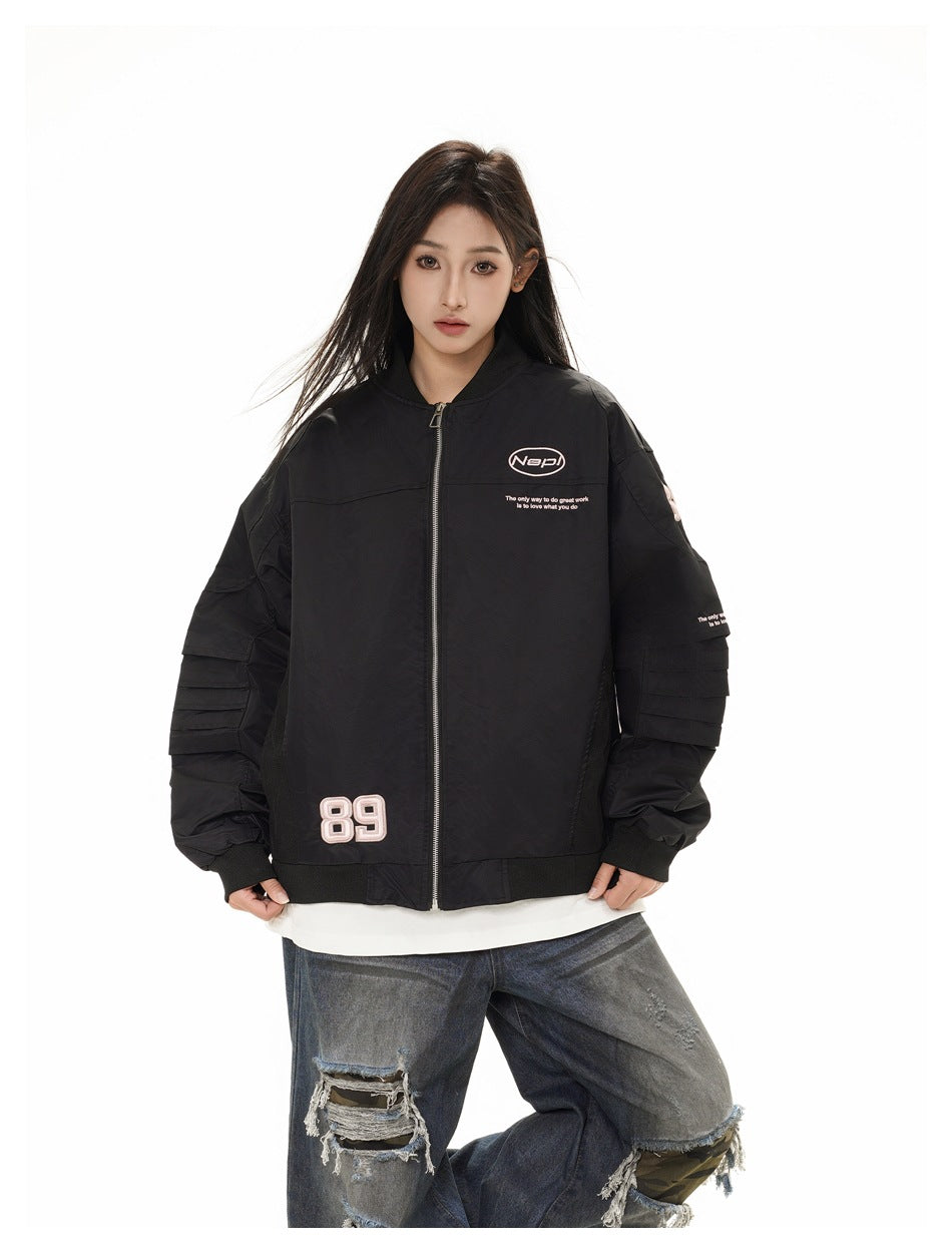 Model wearing an oversized black bomber jacket with pleated sleeves, zipped front and pink 89 patch over ripped jeans