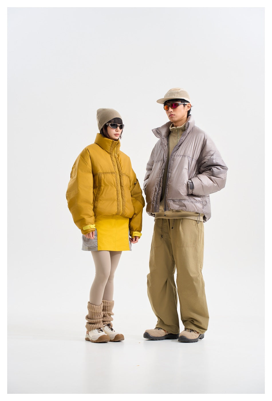 Two models pose in mustard and taupe puffer jackets, shown from a slight angle against a light studio background.
