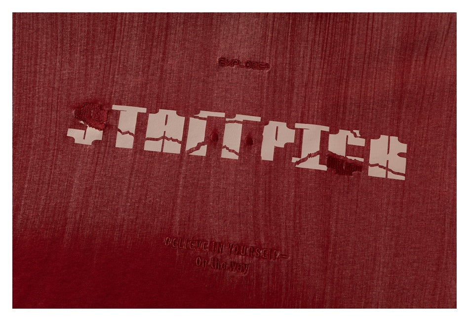 Close-up of a burgundy T-shirt with large pale distressed lettering and small embroidered English text.
