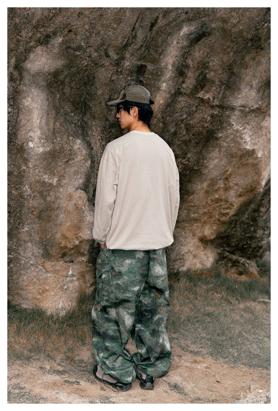 Rear view of a model wearing an oversized beige long-sleeve shirt and loose green camouflage trousers.