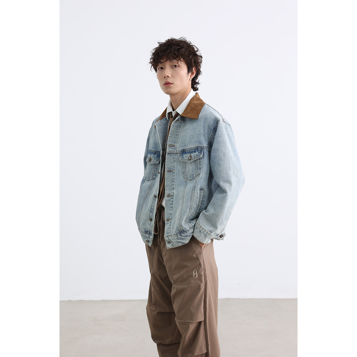 Model wearing a light-wash denim jacket with a brown collar and brown trousers, shown at a three-quarter angle.