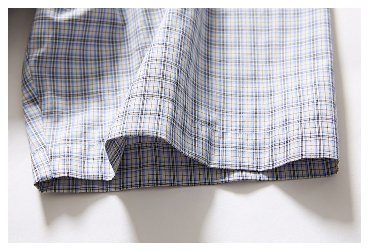 Close-up of the curved bottom hem of a white shirt with a blue and gray plaid pattern.