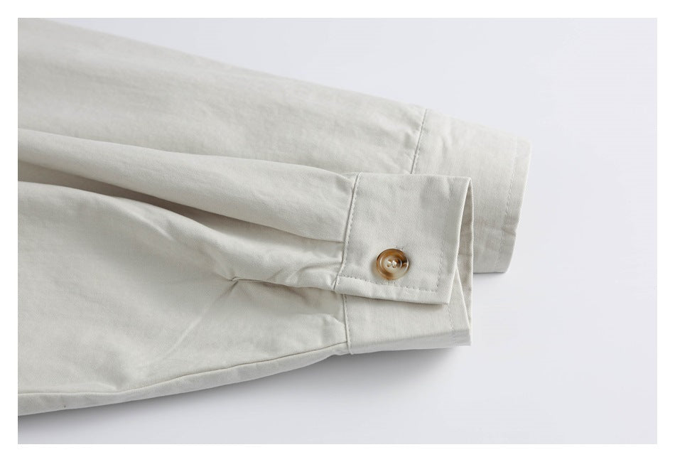 Off-white shirt sleeve cuffs laid flat, showing a tan button and cuff stitching.