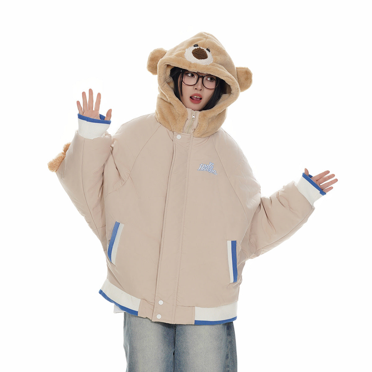 Model wearing a beige hooded jacket with a bear-face hood, blue-and-white trim, and jeans; front view.