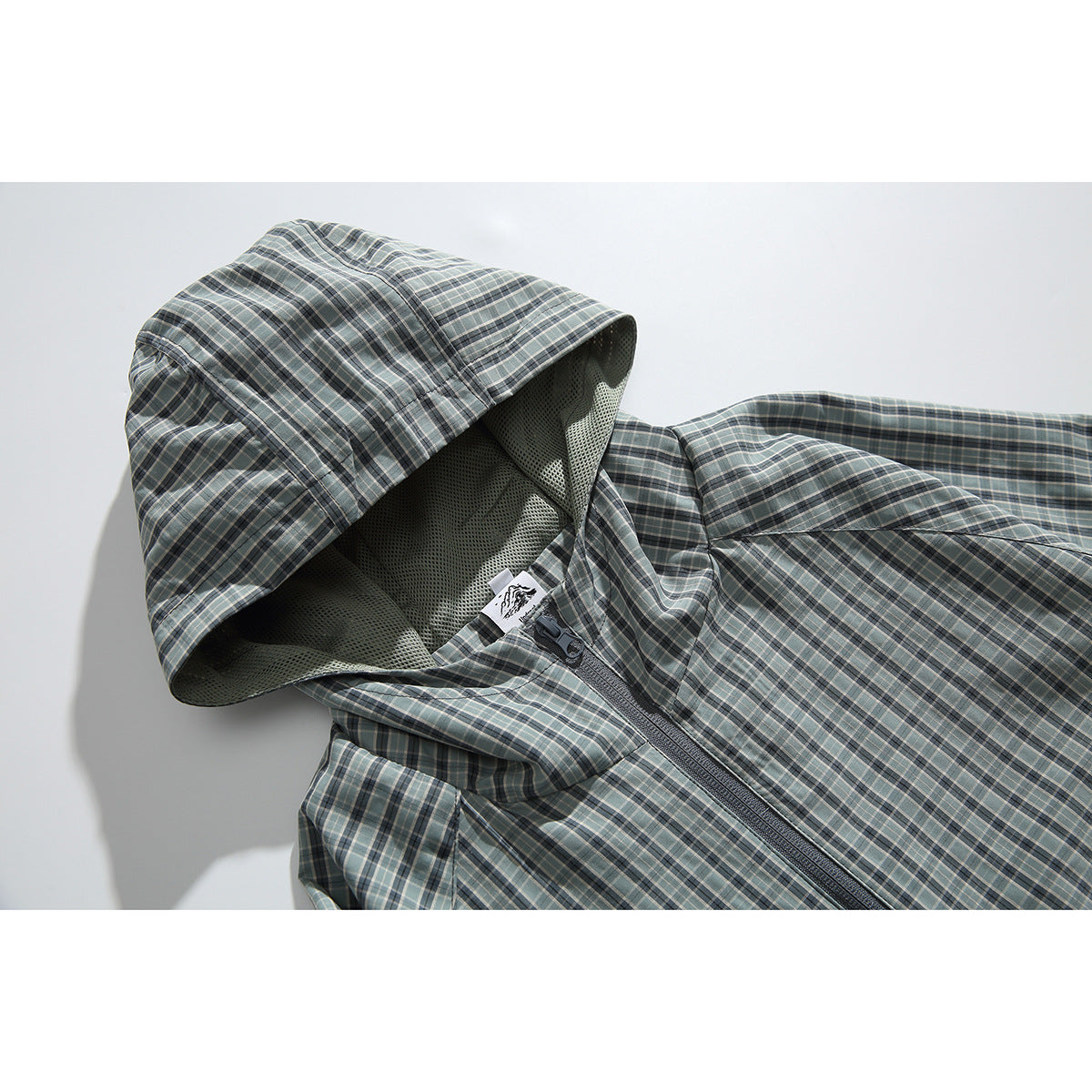 Close-up of a gray-green plaid hooded jacket showing its mesh-lined hood, zipper, and small neck label.
